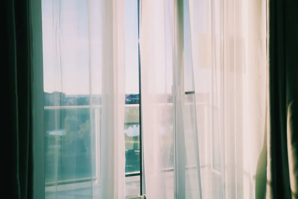 Sheer white curtains moving in front of an open balcony door beside an unmade bed